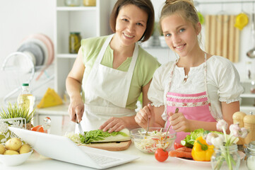 Wall Mural - Cute little girl with mother cooking together at kitchen table