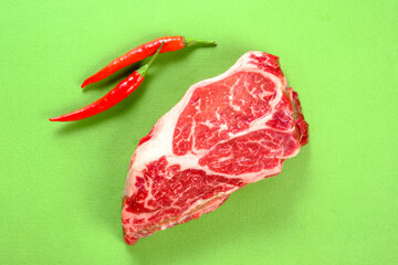 Fresh raw beef steak with red chili pepper on a green background close up