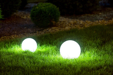 backyard 2 light garden with lantern electric lamp with sphere diffuser in green grass with thuja bushes and stone mulching in park with landscaping, closeup night scene nobody.