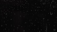 4K Footage Of Rain Drops Falling On Window Glass On Black Background.