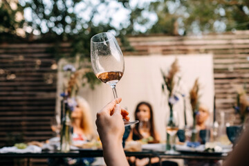 Woman holding a glass of rose wine at an open air party at a restaurant terrace. Wine tasting party with a sommelier.