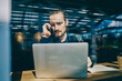 © BullRun - Puzzled male freelancer using smartphone technology for making online call and consultancy about update for laptop system, millennial hipster guy reading received message while phoning via cellular