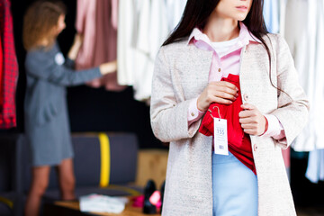 Closeup of young woman is stealing red jeans in store, shop, boutique at shopping center. Girl is hiding unpaid good under clothes. Seller, assistant caught thief on hot. Shoplifting concept.