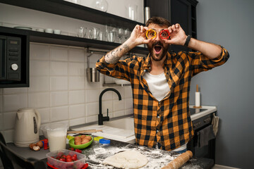 Young man is making cookies in his kitchen. He is having fun with molds.