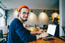 Portrait Of Happy Male Freelancer In Optical Eyewear For Vision Correction Smiling At Camera During Break From Web Working Online, Cheerful Hipster Blogger Sitting In Cafe With Mockup Laptop Computer