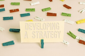 Poster - Conceptual hand writing showing Developing A Strategy. Concept meaning Discussing the Ideas for New Goal Marketing Vision Planning Business Colored clothespin papers empty reminder pink floor office