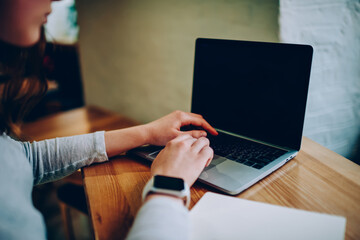 Cropped image of female freelancer using laptop computer for searching information and browsing website on blank monitor,woman using netbook application with mock up screen for e learning in cafe.