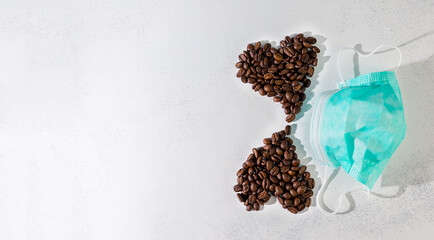 coffee beans laid out in the shape of two hearts on a white scuffed background, with medical masks. The concept of a popular invigorating drink and love in the new normal reality. selective focus.