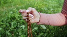 Woman Lit Hand Close Up Counts Rosary - Malas Strands Of Gemstones Beads Used For Keeping Count During Mantra Meditations. Girl Sits On Summer Nature.