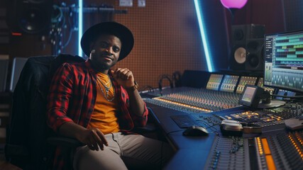 Fototapete - Stylish Audio Engineer Working in Music Recording Studio, Uses Mixing Board and Software to Create Modern Hit Song. Looking at Camera Portrait of Black Artist Musician Working at Control Desk