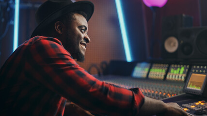 Fototapete - Portrait of Audio Engineer Working in Music Recording Studio, Uses Mixing Board Create Modern Sound. Successful Black Artist Musician Working at Control Desk. Having Fun, Smiling.