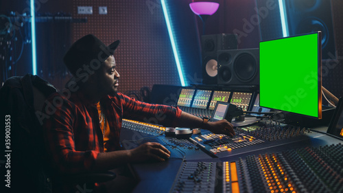 Stylish Audio Engineer Producer Working in Music Record Studio, Uses Green Screen Computer, Mixer Board Equalizer and Control Desk to Create New Hit Track and Song. Artist Musician. Side View Portrait