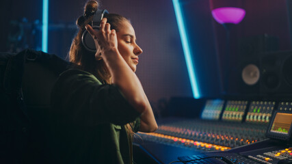 Portrait of Beautiful Female Artist Musician in Music Recording Studio Putting on Headphones. She Uses Mixing Board Create Modern Song. Successful Female Audio Engineer, Producer Working.