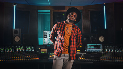 Fototapete - Portrait of Young Black Artist, Musician, Audio Engineer, Producer Wearing Stylish Hat and Standing in Music Record Studio. In the Background Control Desk, Mixing Equipment, Soundproof Room.