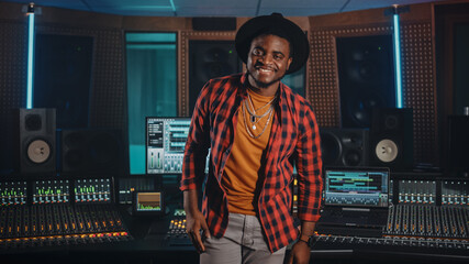 Fototapete - Portrait of Young Black Artist, Musician, Audio Engineer, Producer Wearing Stylish Hat and Standing in Music Record Studio. In the Background Control Desk, Mixing Equipment, Soundproof Room.