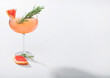 © DenisMArt - Red grapefruit cocktail in modern luxury martini glass with rosemary and fruit slice on white background.