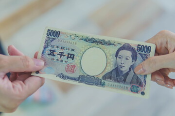 Close up of hand paying or giving cash money Japanese yen banknote to another to person. The yen is the official currency of Japan. Money, loan and corruption concepts
