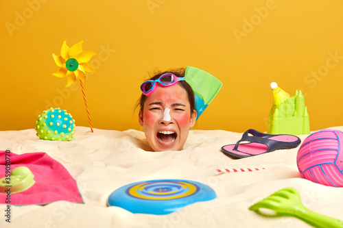 Photographie Emotional young Asian woman spends leisure time at beach, buried in sand, swimmi