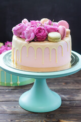 Elegant pink wedding cake decorated with melted white chocolate, beautiful fresh roses and macaroons. Black background.