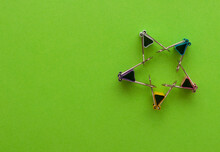 Five Binder Clips Of Different Colors On A Green Paper Background Making Star Figure By Holding Hands, Selective Focus