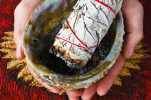 A Close Up Image Of Hands Holding A Abalone Shell And White Sage Smudge Stick. 