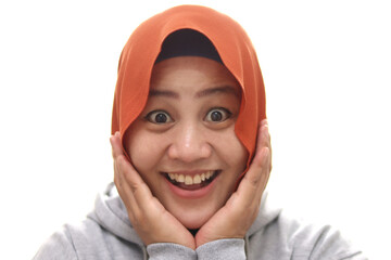 Wall Mural - Young Asian muslim woman wearing hijab with surprised excited happy screaming. Cheerful girl with funny joyful face expression, hands holding face