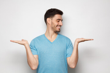 young handsome man choosing between two different options, holding 2 hands, isolated on gray backgro