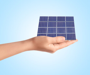 woman demonstrating solar panel on light blue background, closeup. alternative energy source