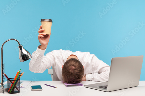 Fotografía Exhausted male employee feeling fatigue lying on table and raising coffee cup, lack of energy in morning office, tired of stress problems sleeping at workplace, overwork concept