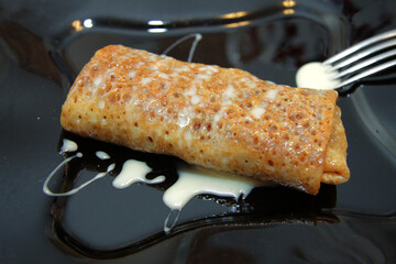 Delicious pancakes filled by fruits on black plate closeup and condensed milk over