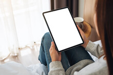 Top View Mockup Image Of A Woman Holding Black Tablet Pc With Blank Desktop White Screen While Sitting On A Cozy White Bed At Home