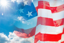 Double Exposure American Flag On The Sunny Sun Flares Blue White Clouds Background. Copy Space For Text.