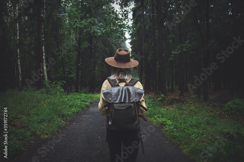 Blonde woman in hat with backpack in rainy day in forest
