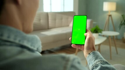 Back View of Woman at Modern Room Sitting on a Chair Using Phone With Green Mock-up Screen Chroma Key Without Track Points Surfing Internet Watching Content Videos Blogs. Double Swipe Up