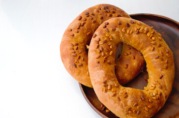 Composition on a light background. Two homemade ruddy bagels with pine nuts on a wooden plate, and on the left there is an empty place for inscription