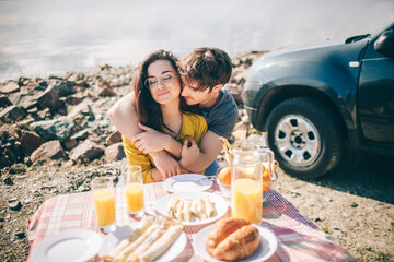 Wall Mural - Picnic near the water. Happy family on a road trip in their car. Man and woman are traveling by the sea or the ocean or the river. Summer ride by automobile.