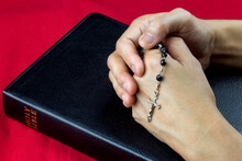 Clasped Hands With Rosary On Closed Bible