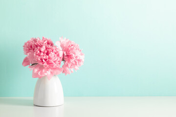 Home decoration with floral decor on table. Beautiful flowers pink peonies in vase on mint background