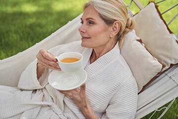 Wall Mural - Joyful mature female relaxing in yard with tea