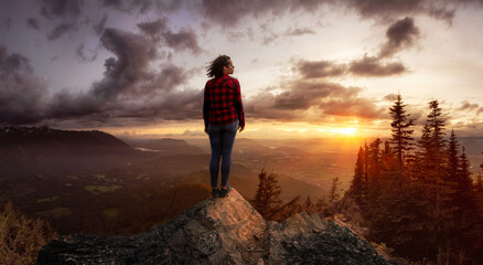 Wall Mural - Fantasy Adventure Composite with a Girl on top of a Rock Cliff with Beautiful Nature Landscape in Background during Sunset or Sunrise. Concept: Hike, Freedom, Explore, Journey