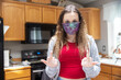 © Mat Hayward - Girl wearing a Covid-19, Coronavirus protection cloth mask in the kitchen and flipping off the camera as a rude gesture