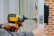 © ungvar - Handyman using a drill to installing lock in door in a house