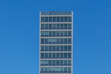 Wall Mural - Outdoor sunny exterior elevation side view of Modern office tower with simply grid frame windows facade against background of blue sky.   