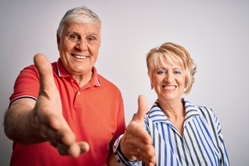 Wall Mural - Senior beautiful couple standing together over isolated white background smiling friendly offering handshake as greeting and welcoming. Successful business.
