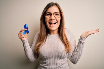 Canvas Print - Young blonde woman holding prostate cancer awareness campaing blue ribbon very happy and excited, winner expression celebrating victory screaming with big smile and raised hands