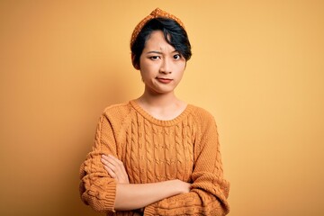 Poster - Young beautiful asian girl wearing casual sweater and diadem standing over yellow background skeptic and nervous, disapproving expression on face with crossed arms. Negative person.