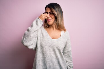 Sticker - Young beautiful brunette woman wearing casual sweater and glasses over pink background smelling something stinky and disgusting, intolerable smell, holding breath with fingers on nose. Bad smell