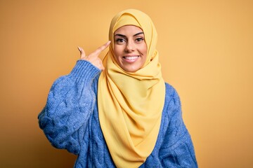 Sticker - Young beautiful brunette muslim woman wearing arab hijab over isolated yellow background Smiling pointing to head with one finger, great idea or thought, good memory