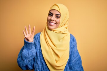 Canvas Print - Young beautiful brunette muslim woman wearing arab hijab over isolated yellow background showing and pointing up with fingers number four while smiling confident and happy.