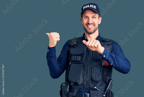 Young handsome man wearing police uniform pointing to the back behind with hand and thumbs up, smiling confident